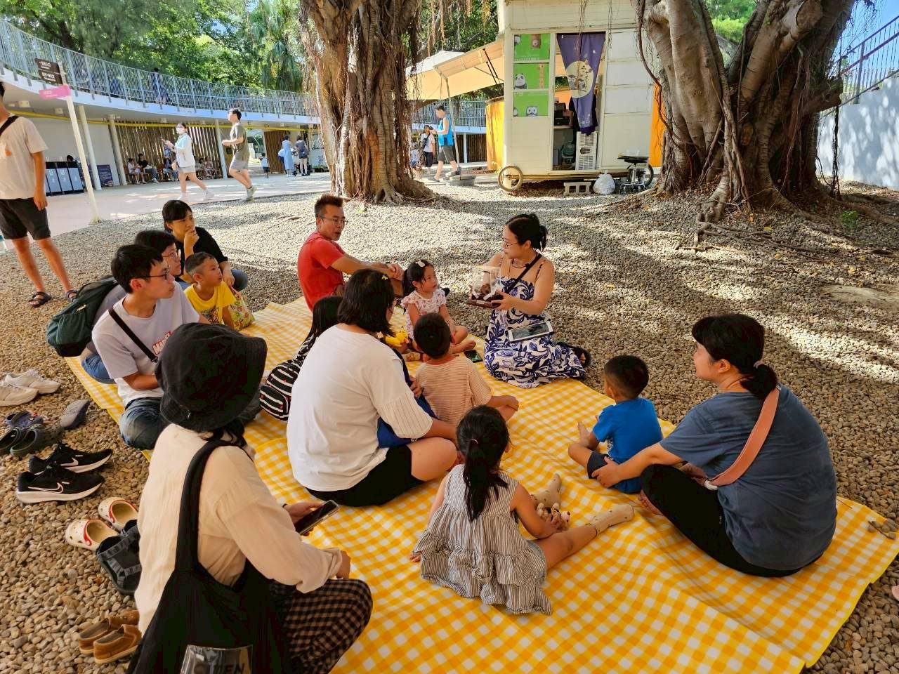 Families listening to a talk on picnic mats under a big tree